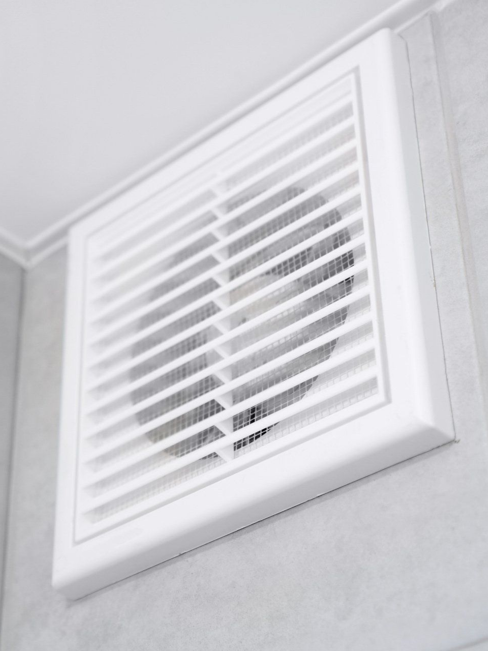 Ventilateur blanc à lamelles, fixé sur un mur gris.