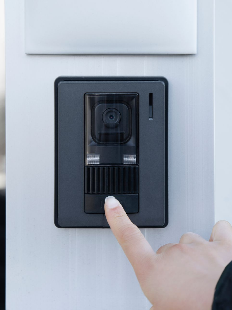 Une main appuie sur une sonnette noire, filmée par une caméra.