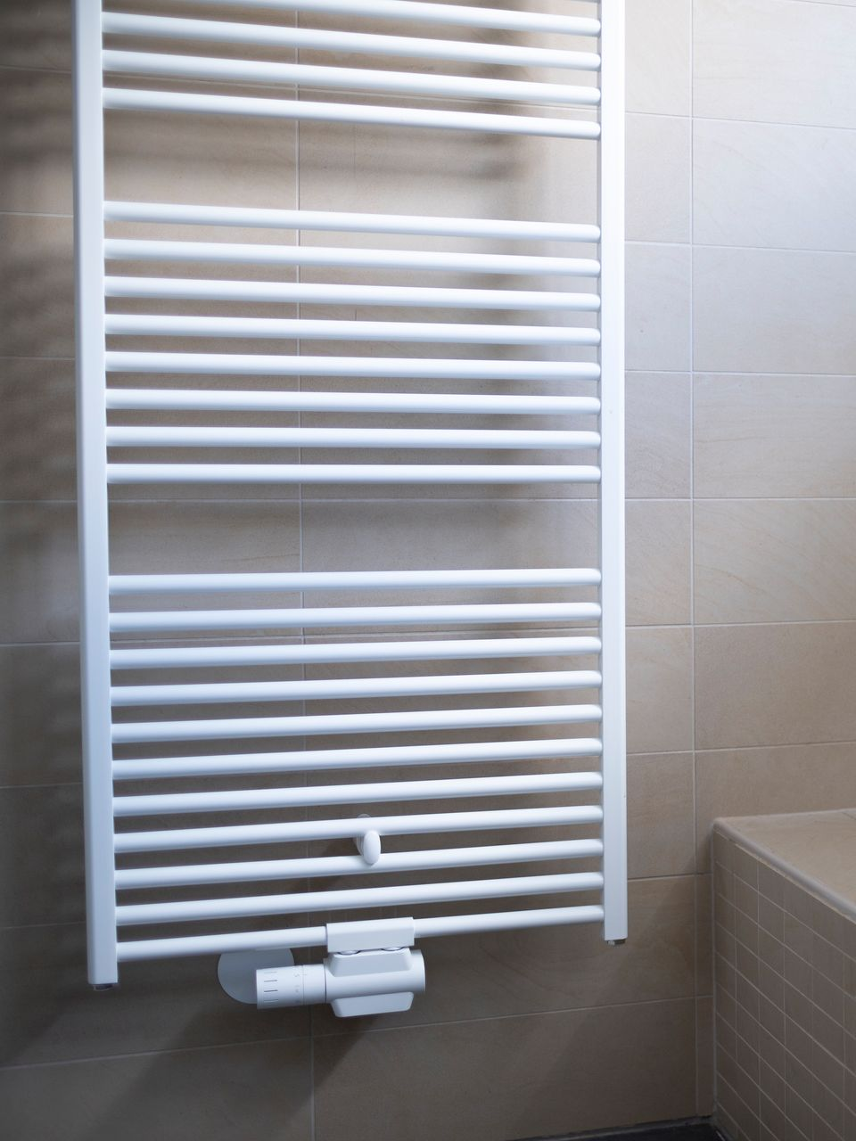 Sèche-serviettes blanc fixé sur un mur carrelé beige dans une salle de bains.