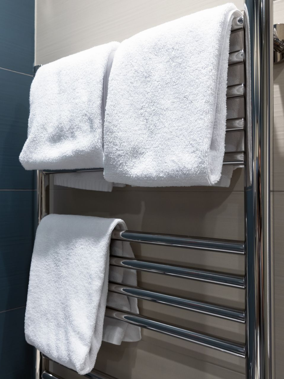 Des serviettes blanches sont suspendues à un porte-serviettes chauffant argenté dans une salle de bains.