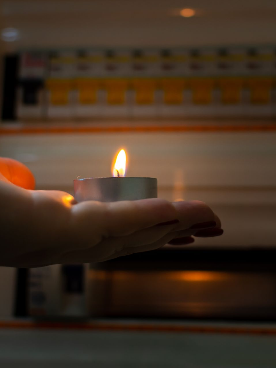 Une main tenant une bougie chauffe-plat allumée devant un tableau électrique dans un environnement sombre.