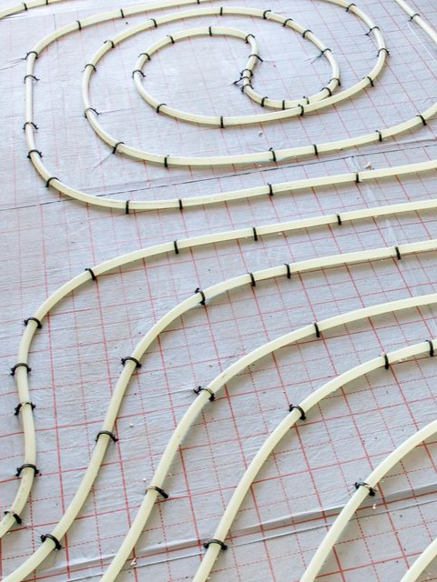 Tuyaux blancs pour chauffage au sol radiant, fixés à une grille rouge sur le sous-plancher.