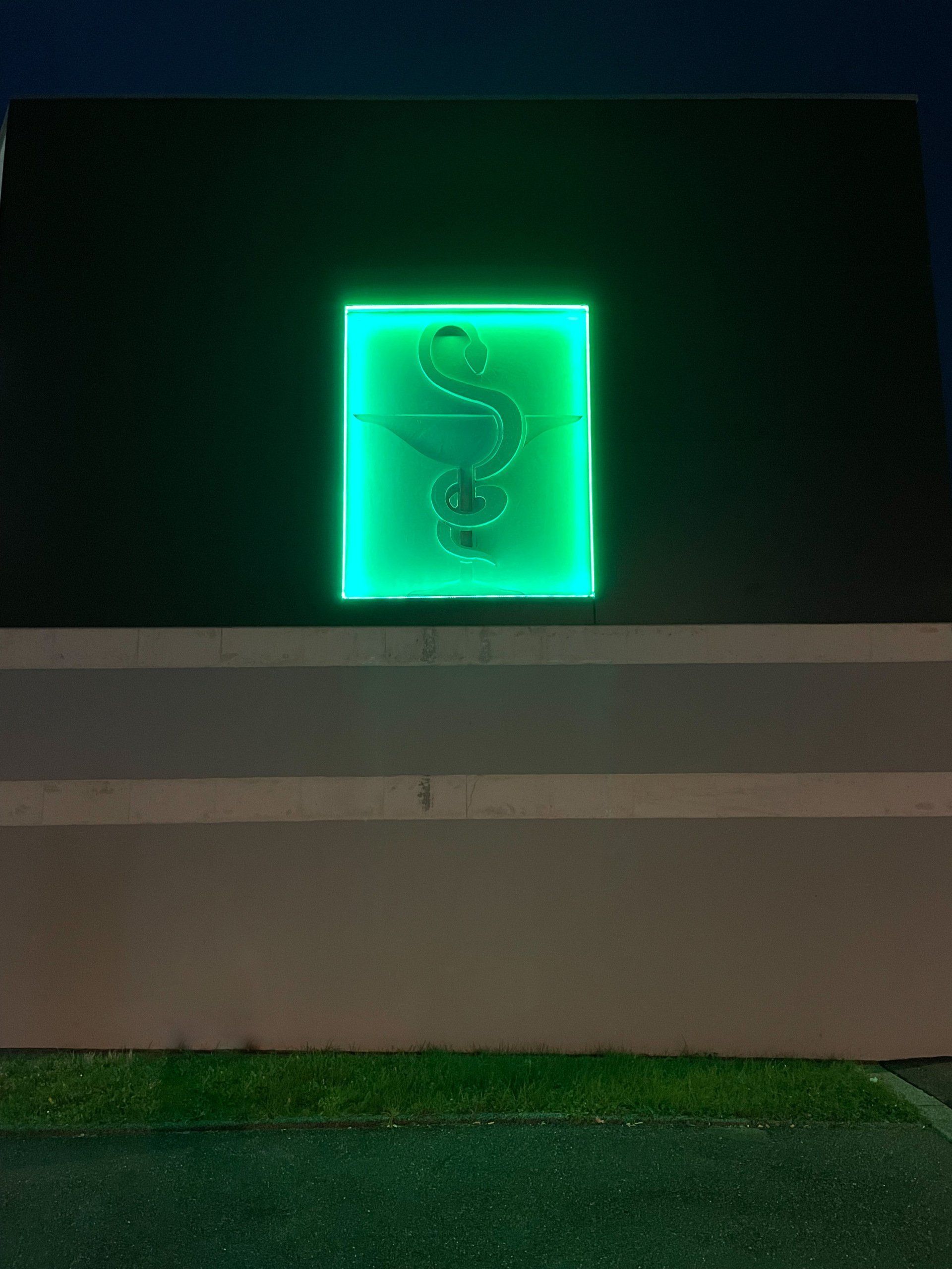 Symbole vert fluo d'une pharmacie sur un mur sombre.
