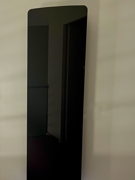 Objet noir rectangulaire aux coins supérieurs arrondis, reflétant la lumière sur un fond blanc.