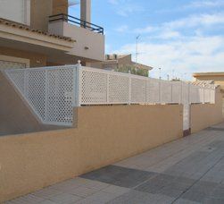 Una valla blanca rodea un edificio al lado de una acera.