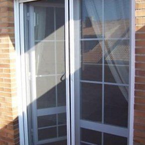 Una puerta corrediza de vidrio con una mampara está en un edificio de ladrillos.