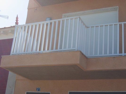 Un balcón con barandilla blanca en el lateral de un edificio.