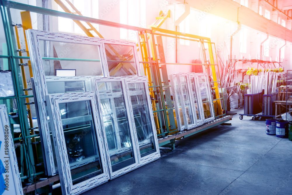 Weiss gerahmte Fenster, hell erleuchtet, lehnen an Regalen in einer Fabrik.