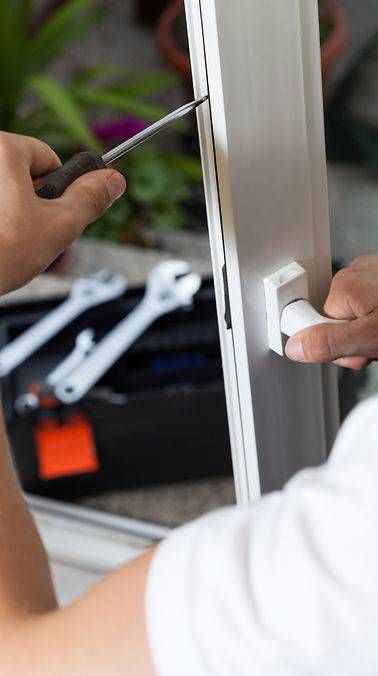 Eine Person benutzt einen Schraubenzieher an einem weissen Fensterrahmen; im Hintergrund sind ein Werkzeugkasten und Werkzeuge zu sehen.