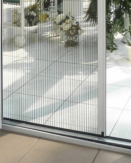 Schiebetür aus schwarzem Netzgewebe verdeckt die Terrassentüröffnung; Licht spiegelt sich auf dem Boden; Pflanzen sind sichtbar.