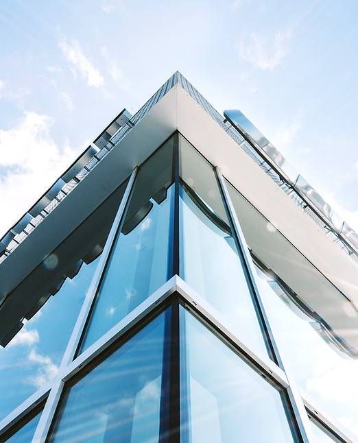 Ecke eines modernen Gebäudes mit Glasfenstern, die den Himmel spiegeln.