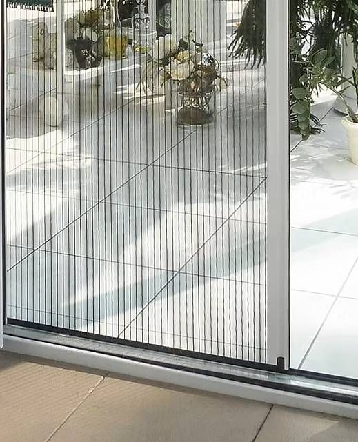 Schiebetür mit Fliegengitter, plissiert, grau mit silbernem Rahmen, öffnet sich zu einer Terrasse.