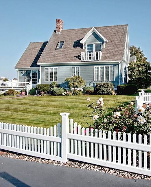 Blaues Haus mit weissem Lattenzaun, grünem Rasen und klarem blauen Himmel.