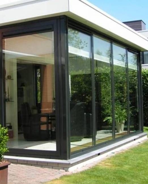 Verglaster Wintergarten mit dunklen Rahmen, weissem Dach und Blick ins Innere und ins Grüne.