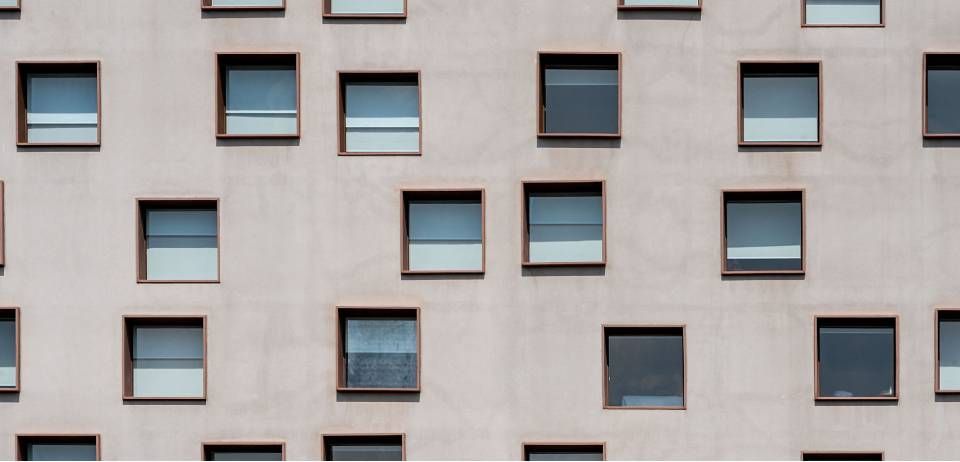 Nahaufnahme einer Gebäudefassade mit zahlreichen quadratischen Fenstern in verschiedenen Blau- und Grautönen.