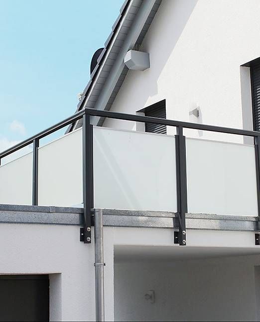 Balkon mit Milchglasscheiben und schwarzem Geländer, an ein weisses Gebäude angebaut.