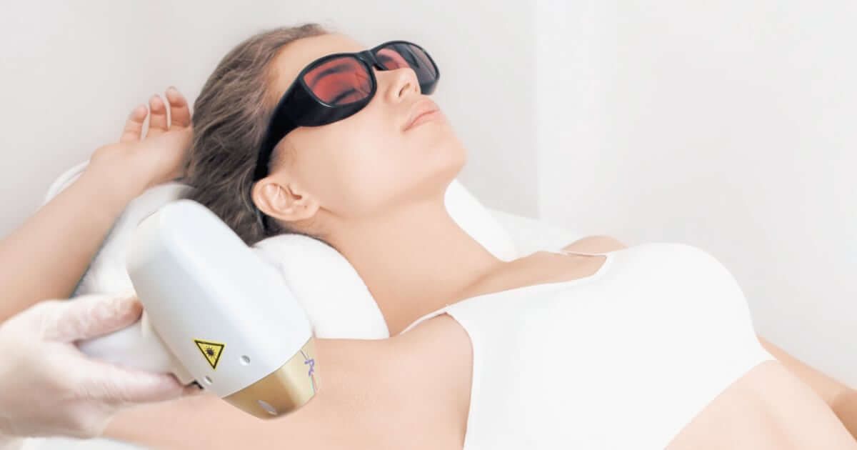 Una persona que lleva gafas protectoras recibe un tratamiento de depilación láser en las axilas en un entorno clínico.
