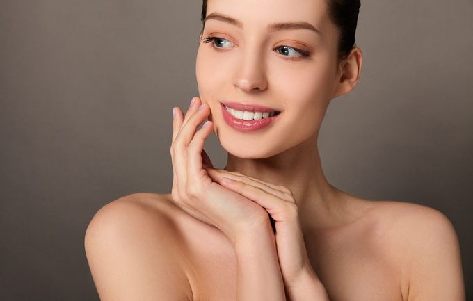 Una persona sonriente, vestida con una bata blanca, se aplica crema 