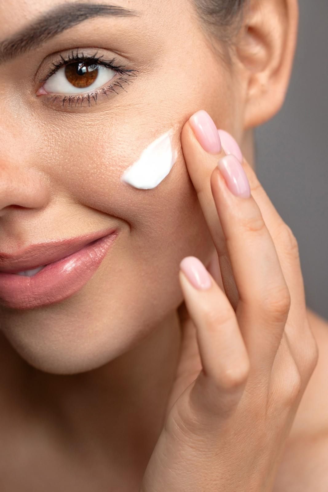 Primer plano de una mano aplicando crema blanca en una mejilla suave.