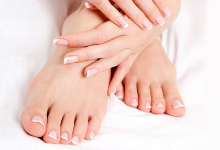 Un par de pies con uñas pintadas al estilo francés, descansando sobre una superficie blanca