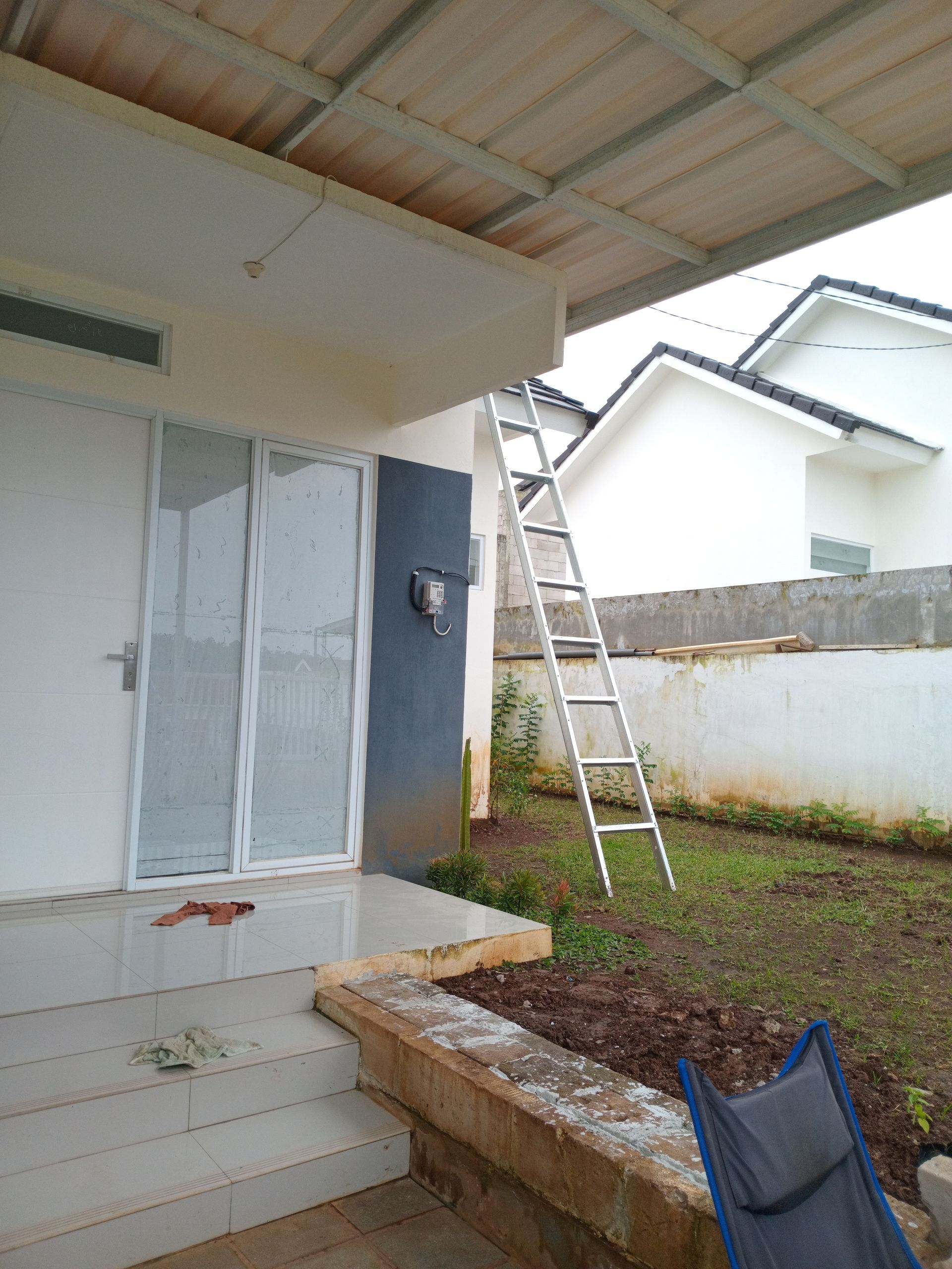 Un parterre de fleurs éclatant, aux teintes roses, jaunes et orange, borde une pelouse verte devant une maison grise.
