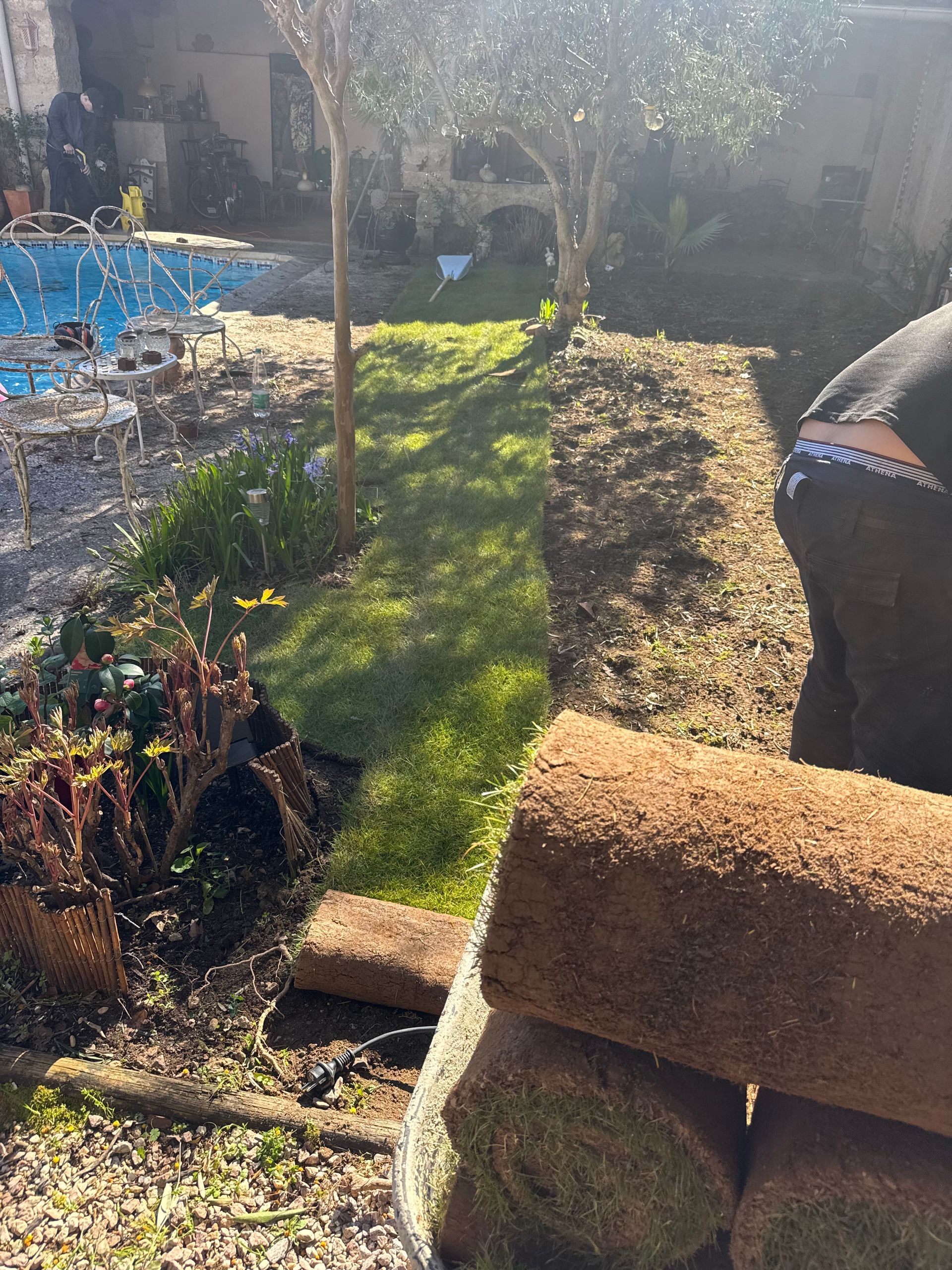 Un champ herbeux avec une tondeuse à gazon au premier plan, menant à un petit hangar et une clôture sous un ciel partiellement nuageux.