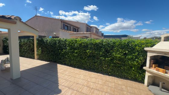 Une parcelle incurvée de gazon artificiel vert, bordée de gravier blanc, jouxte un bâtiment beige sous un ciel bleu.