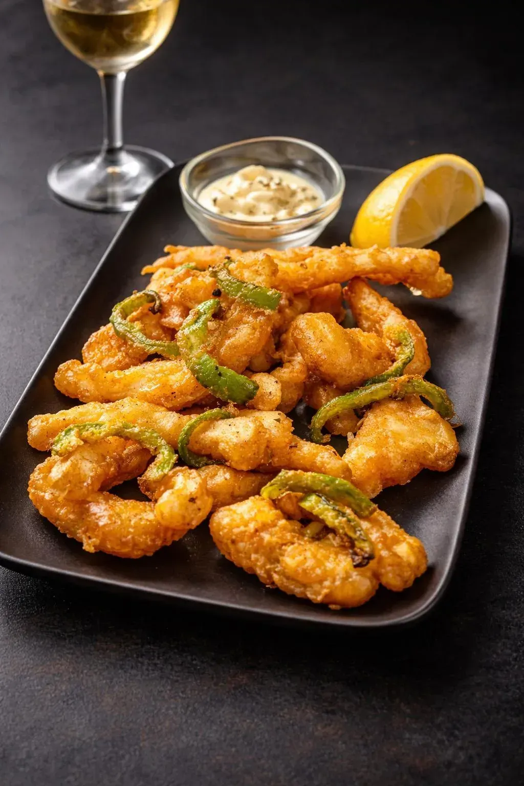 Una fuente rectangular rellena de ensalada de patatas cremosa, cubierta con tiras de pimiento rojo y aceitunas verdes.