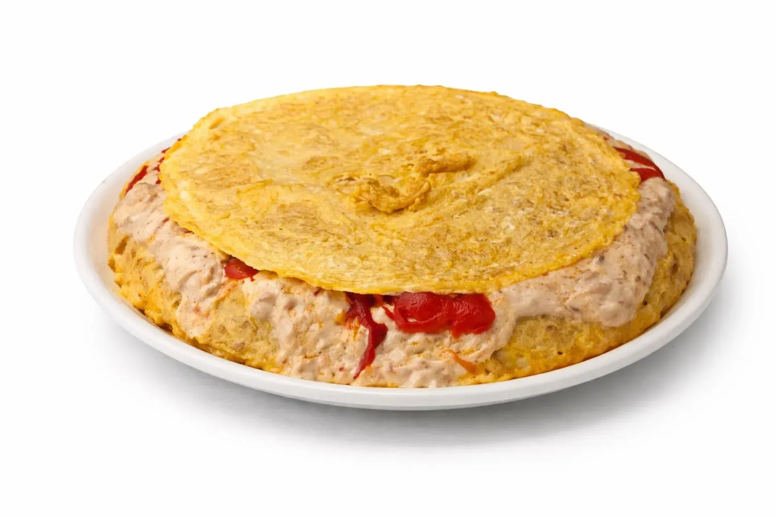 Una tortilla dorada y circular servida en un plato blanco con un relleno de ensalada de atún cremosa con motas rojizas.