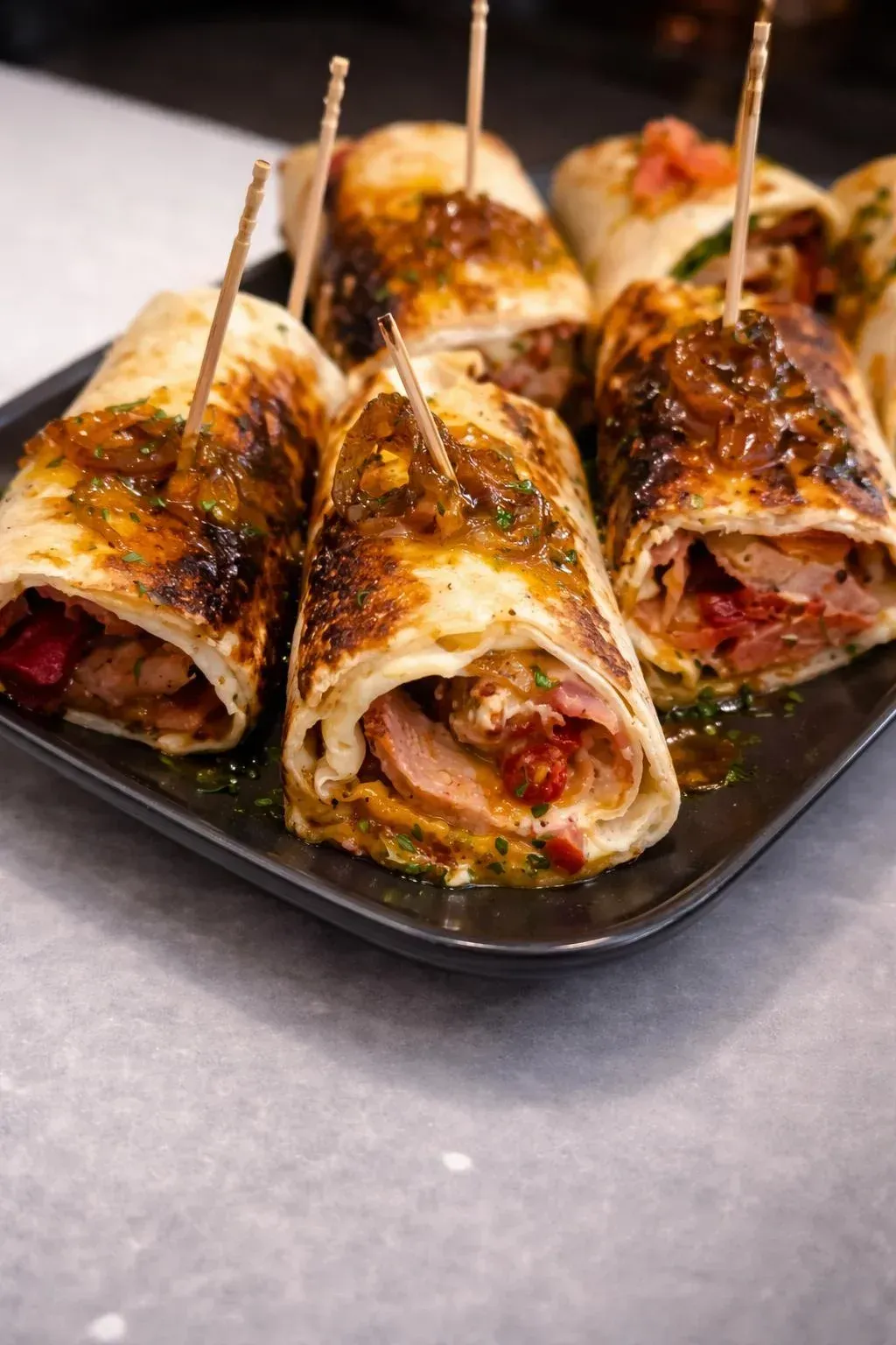 Un plato rectangular negro contiene varios rollitos de tortilla dorados