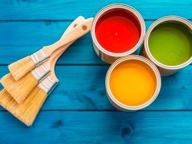 Tres latas de pintura y tres pinceles sobre una mesa de madera azul.