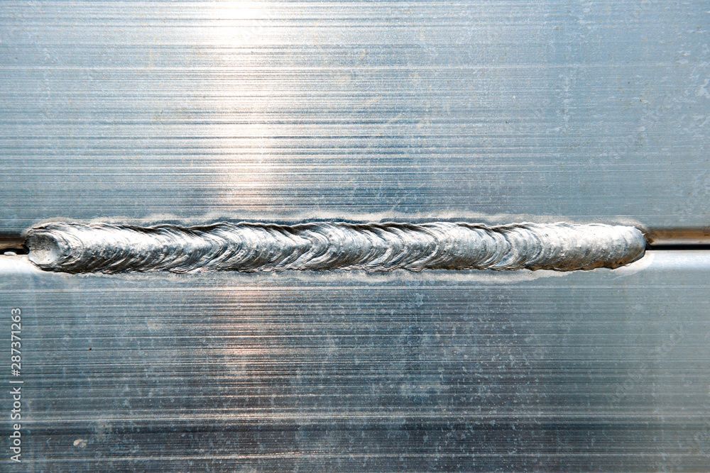 Eine Nahaufnahme einer silbernen Schweissnaht, die zwei Metallplatten verbindet, zeigt die wellenförmige Schweissnaht.