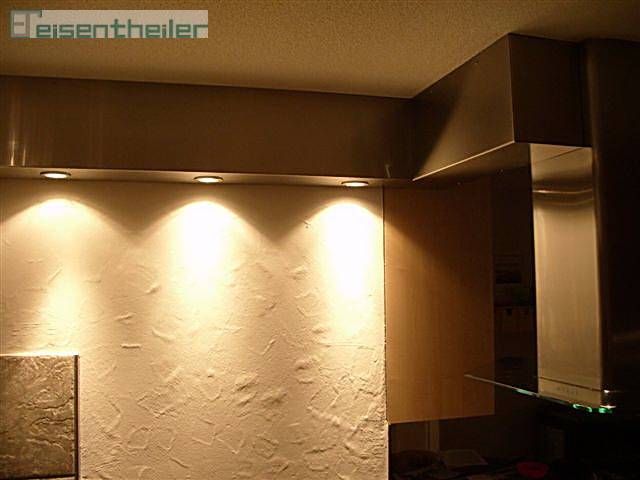 Küchenwand mit Einbauleuchten, strukturierter Oberfläche und Dunstabzugshaube aus Edelstahl.