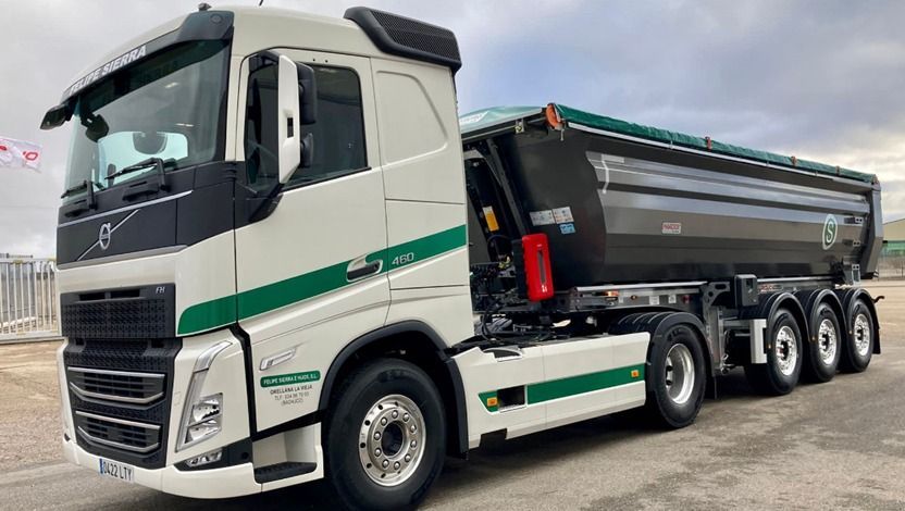 Camión Volvo blanco con caja de volteo negra y detalles en verde, estacionado al aire libre.