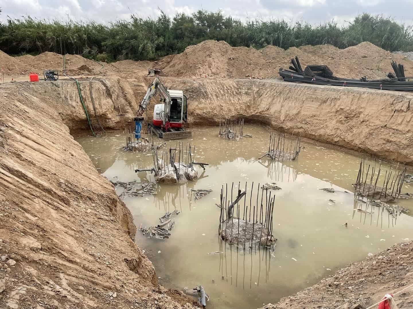 Excavación en obra con maquinaria y agua estancada. Entorno fangoso y marrón.