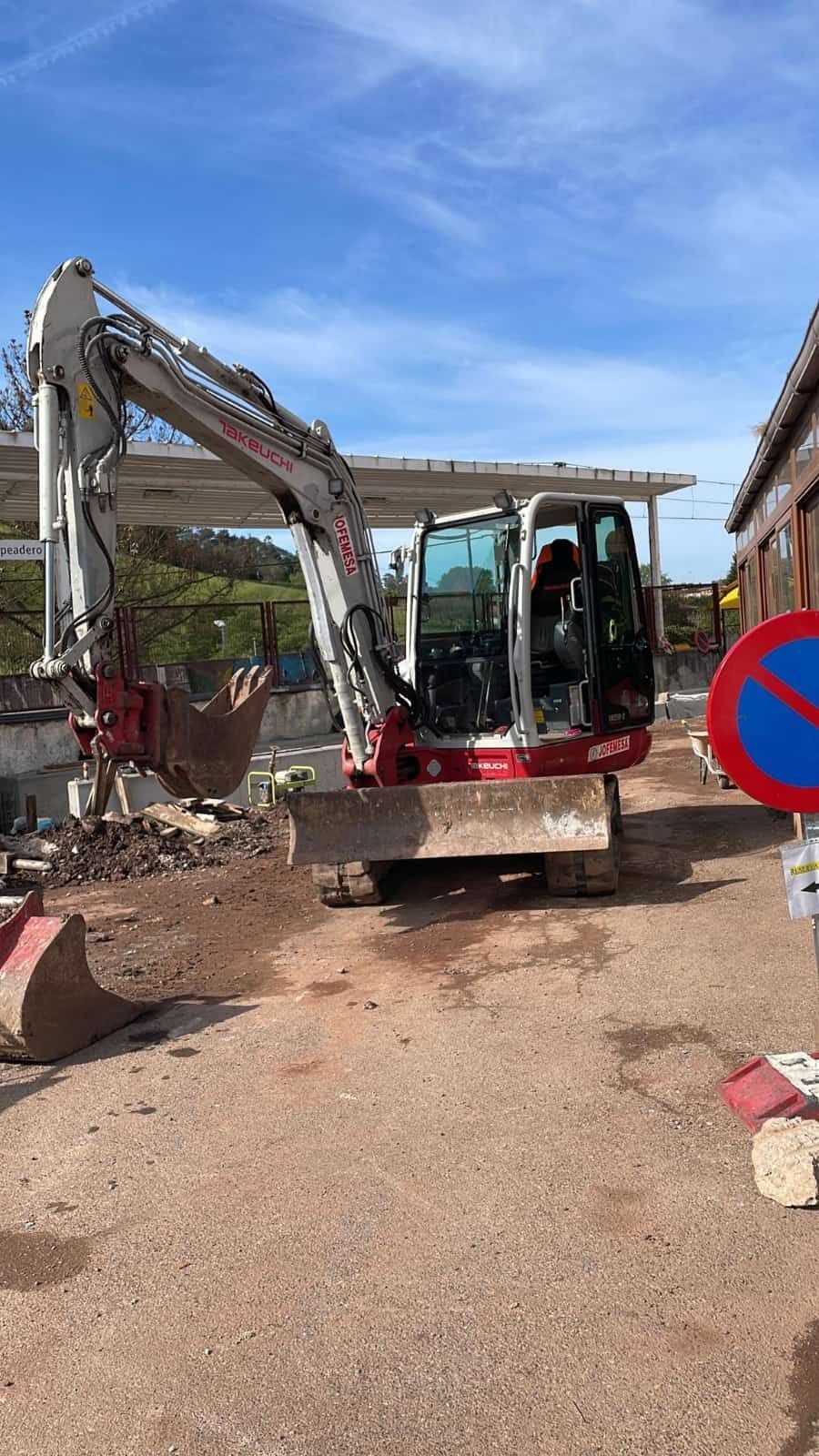Excavadora en funcionamiento en una obra; maquinaria roja, blanca y gris. Señal de prohibido detenerse y cielo azul de fondo.