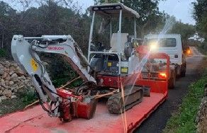 Miniexcavadora en un remolque rojo, siendo remolcada por un camión en una carretera.