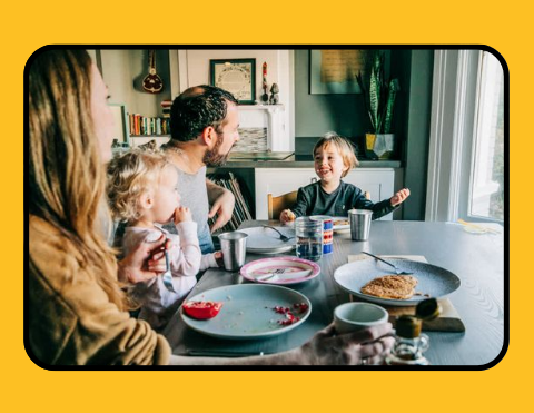 Una familia está sentada en una mesa comiendo comida.