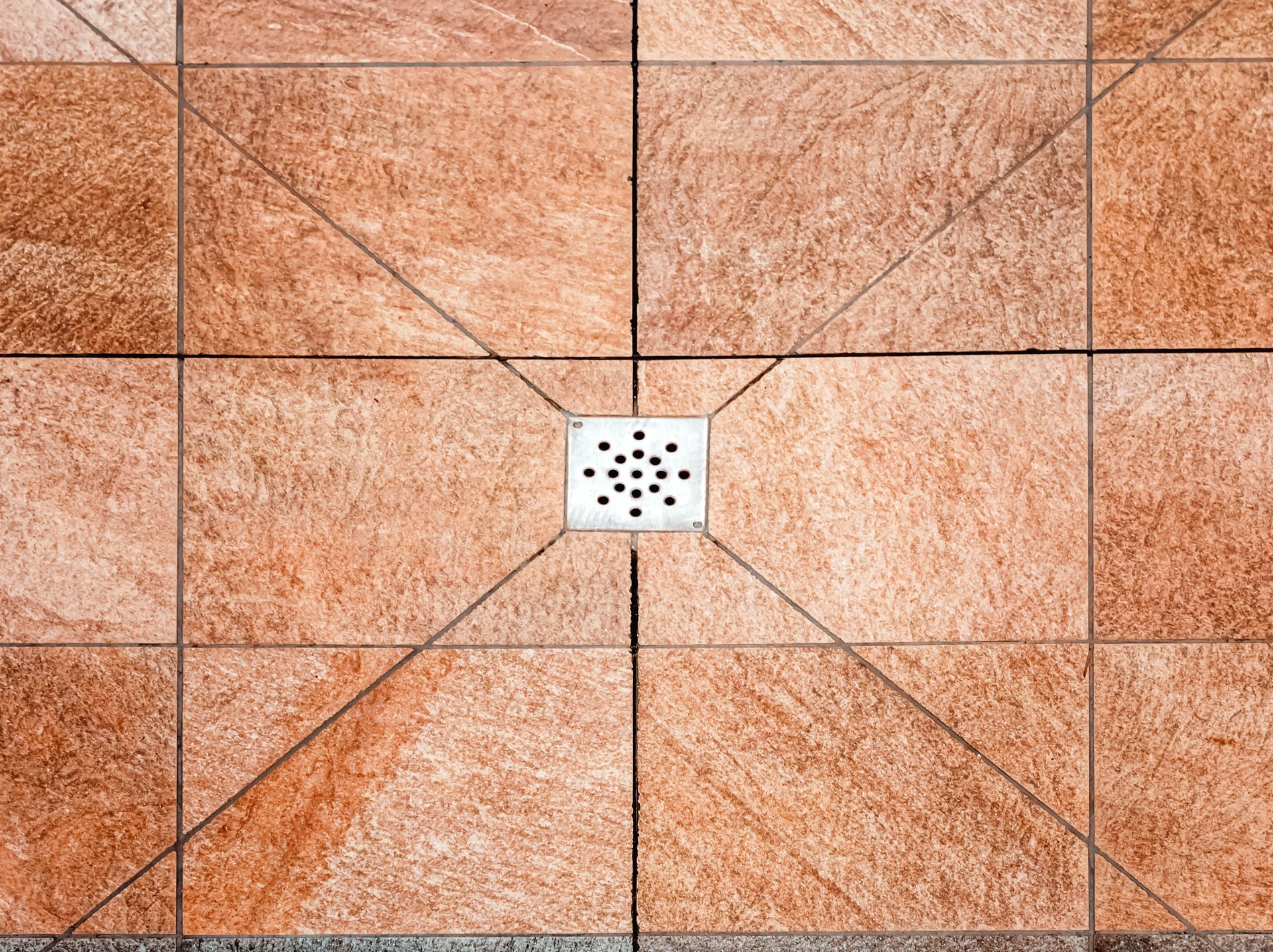 Gros plan sur un sol carrelé orange avec une petite grille d'évacuation carrée au centre.