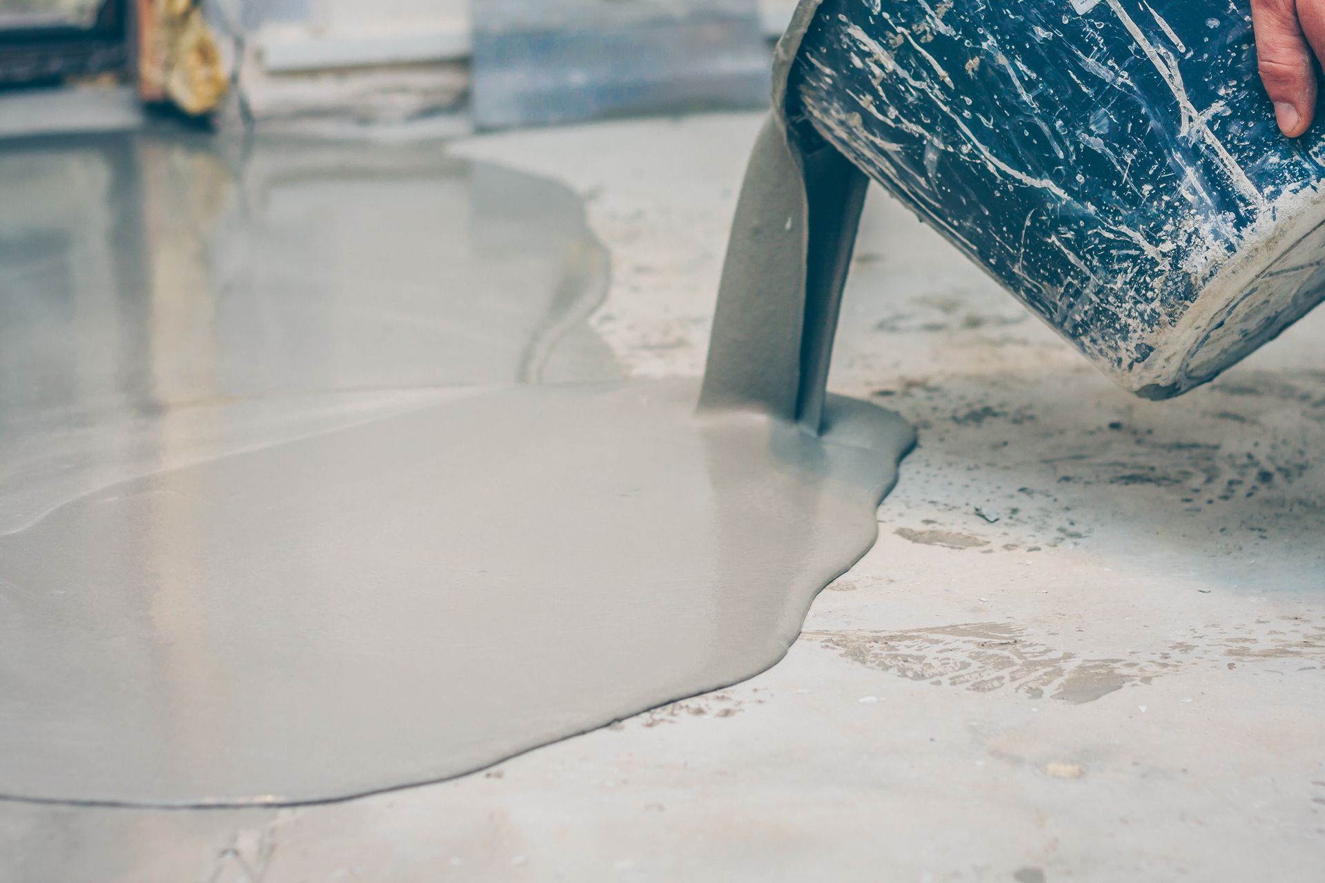 Un artisan fait couler une chape liquide grise au sol.