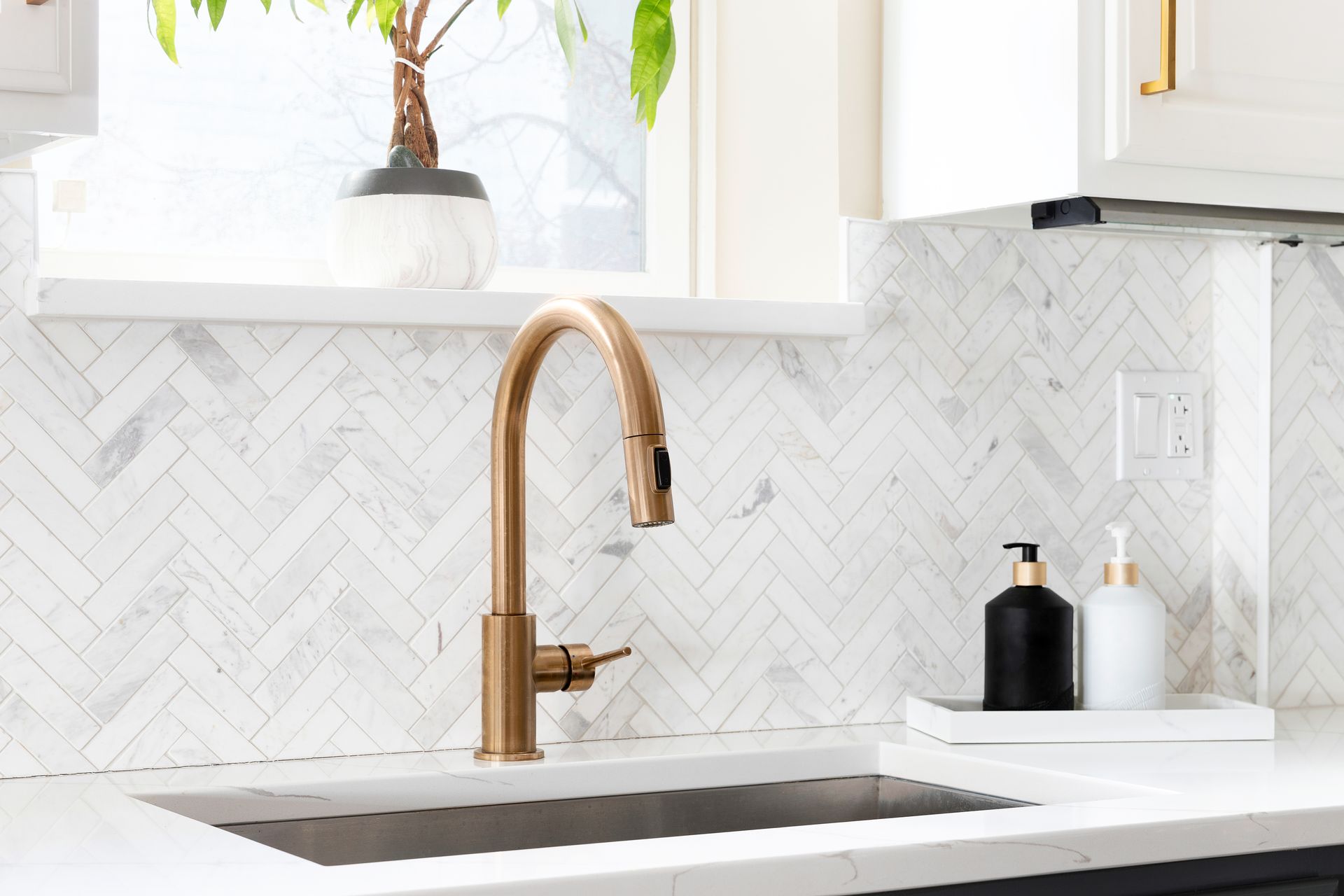 Lavabo de cuisine avec robinet doré et crédence carrelée.