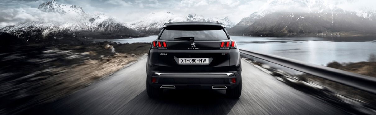 Un SUV noir roule sur une route avec des montagnes et de l'eau en arrière-plan.