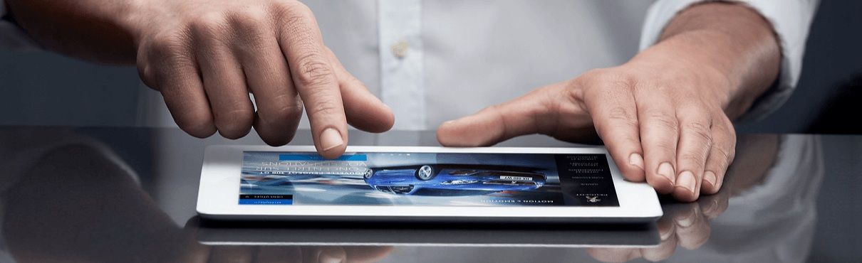 Des mains manipulent une tablette, probablement en train de consulter une page web avec une image de voiture. 