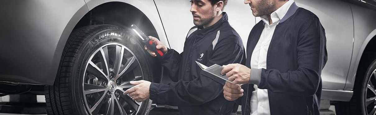 Un mécanicien et un client près d'une roue de voiture, le mécanicien montre du doigt, le client observe.