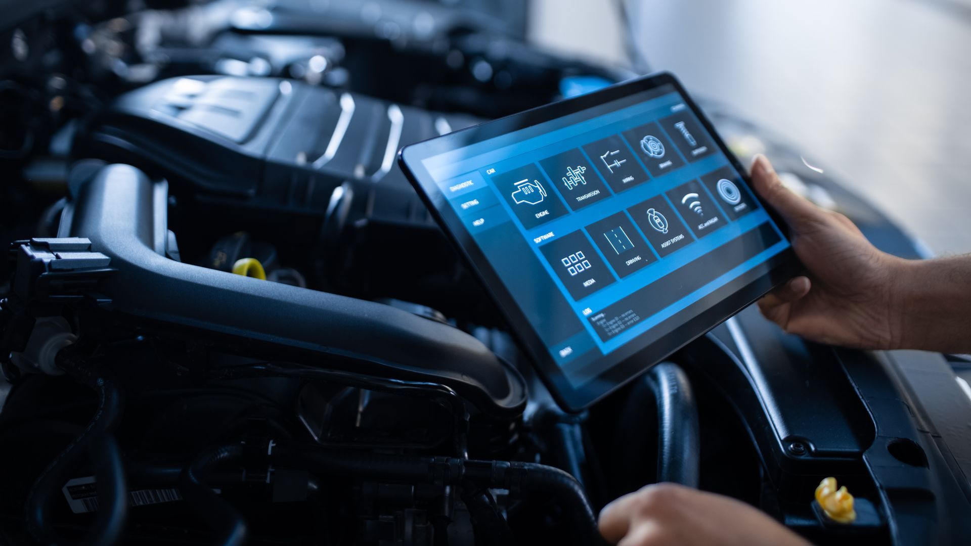 Une personne utilise une tablette pour diagnostiquer le moteur d'une voiture. La tablette affiche des icônes de diagnostic, avec le moteur visible en arrière-plan.