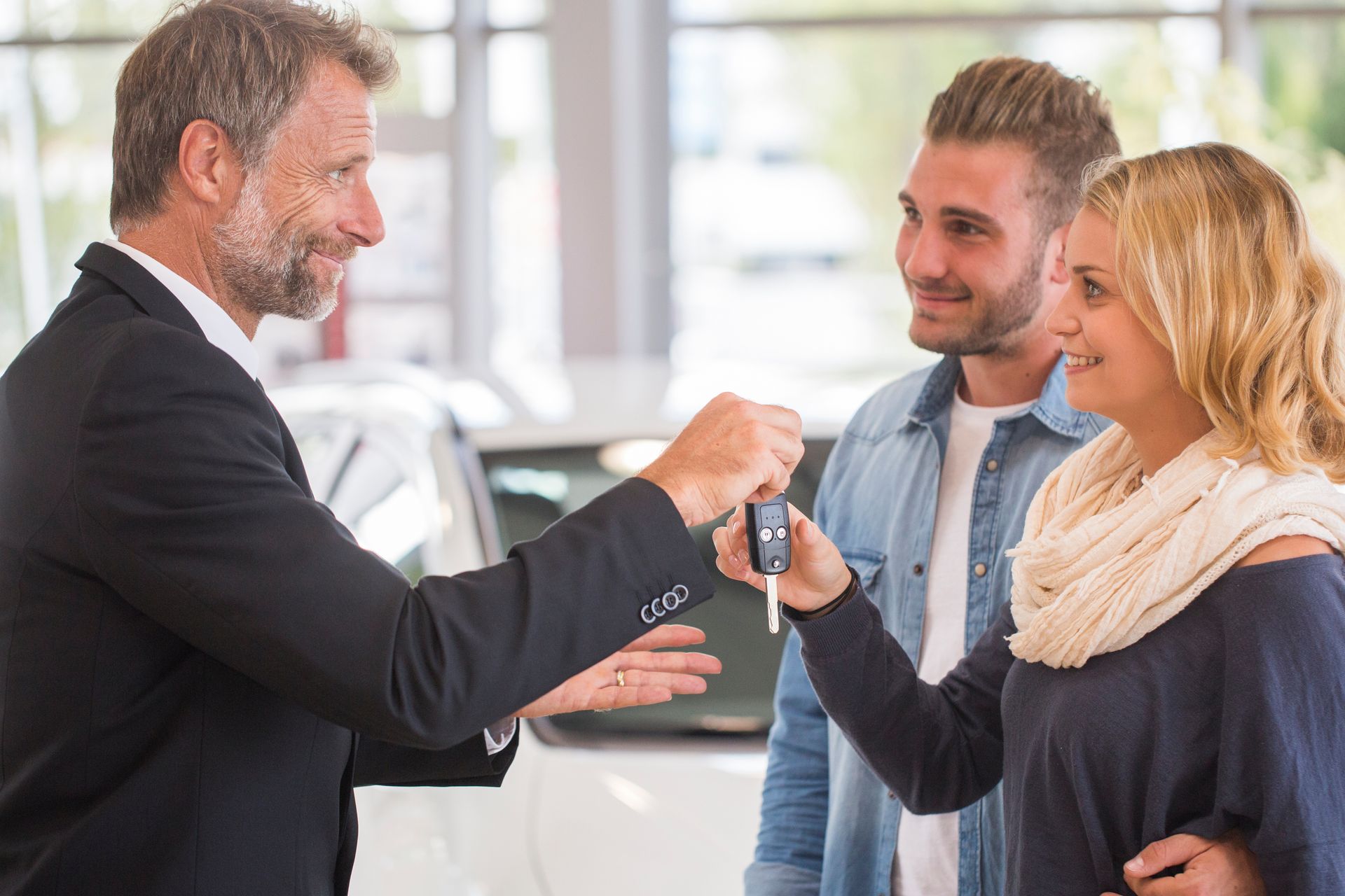 Un vendeur de voitures remet des clés à un couple souriant chez un concessionnaire automobile.