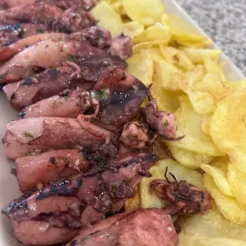 Calamares a la plancha con patatas fritas en un plato, con tentáculos chamuscados y patatas fritas doradas.