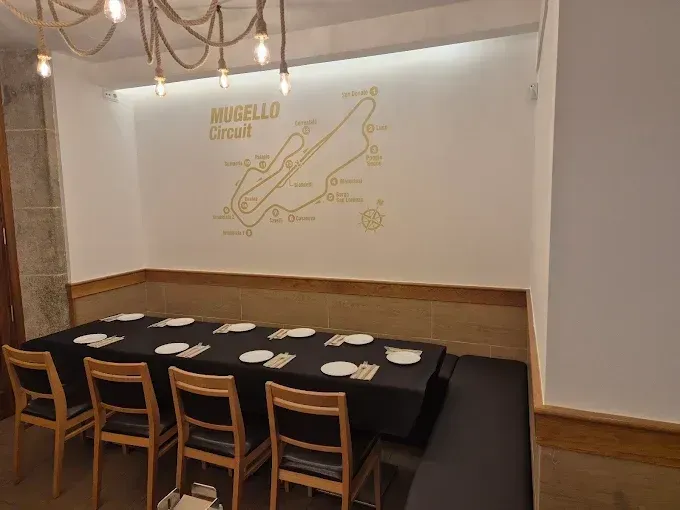 Comedor del restaurante con una mesa larga negra, sillas de madera y un mural en la pared.