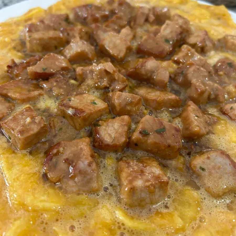 Primer plano de carne cortada en dados chisporroteando en una tortilla o salsa amarilla, con aceite burbujeante.