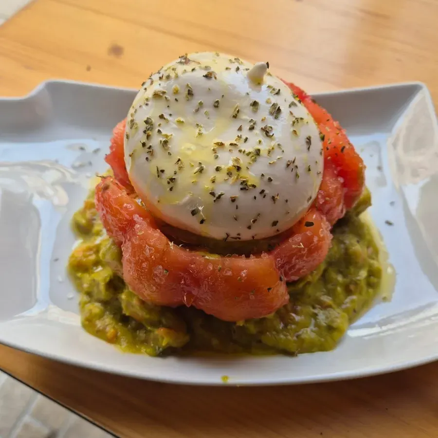 Tomate picado y salsa verde coronados con un huevo escalfado en un plato blanco.